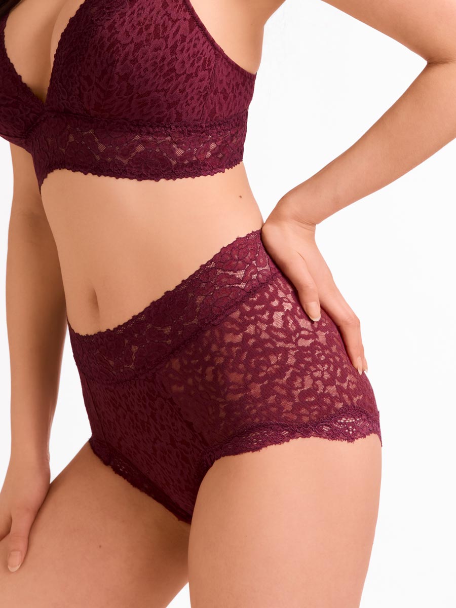Woman wearing a burgundy/maroon lace bra and shortie on a white background